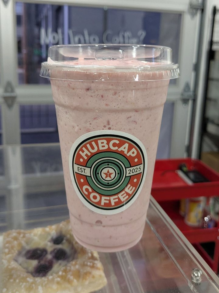 A pink strawberry frappe in a Hubcap cup on the pastry case, next to a blueberry danish