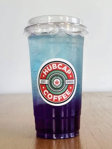 An iced drink that fades from bright blue at the top to purple at the bottom, in a Hubcap cup