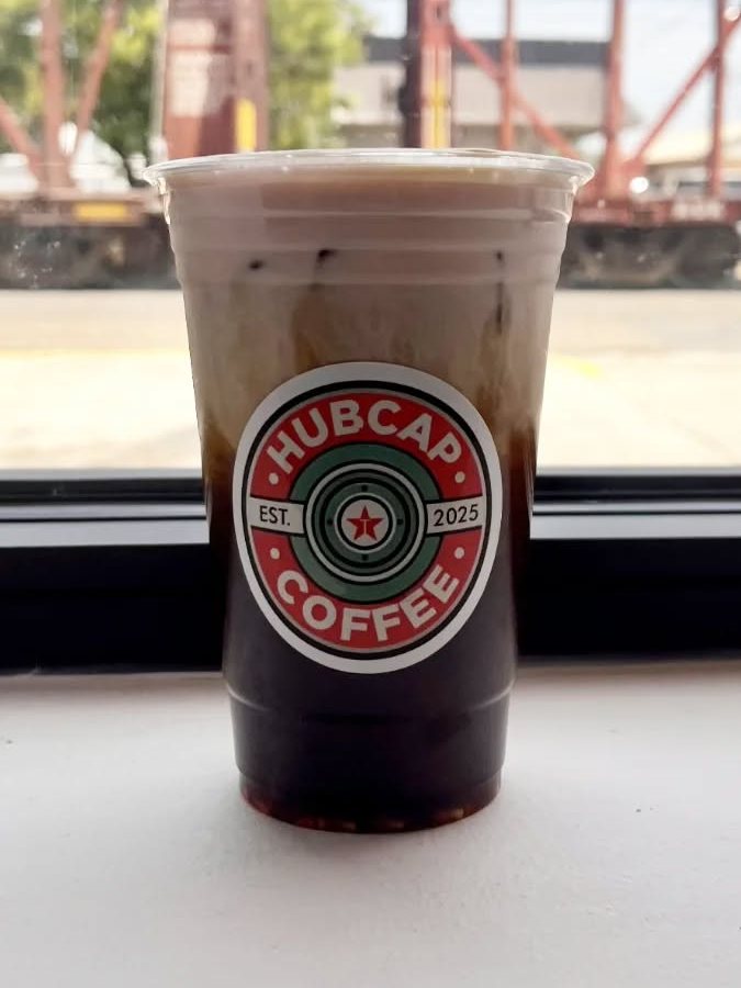 An iced latte on the front windowsill with a freight train on the tracks outside