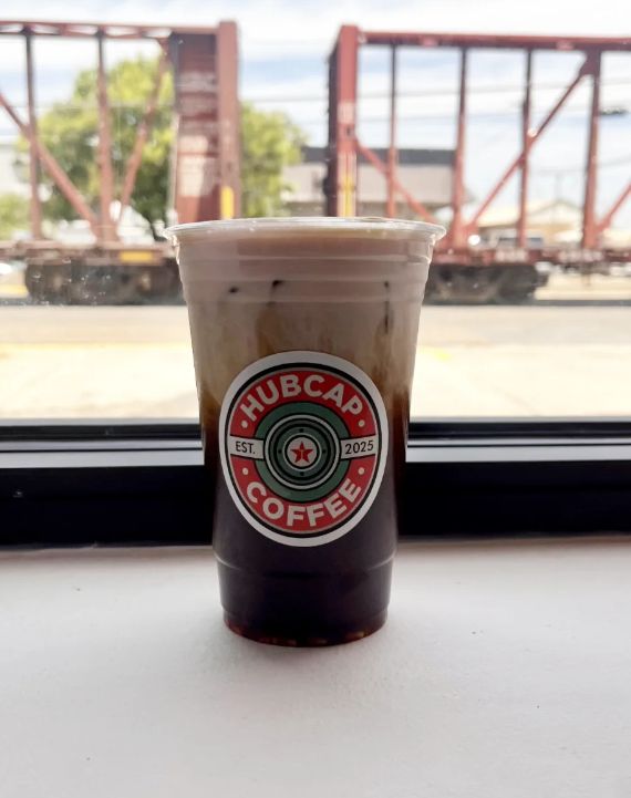 An iced latte in a Hubcap Coffee cup on the front windowsill, with a freight train passing on the tracks outside