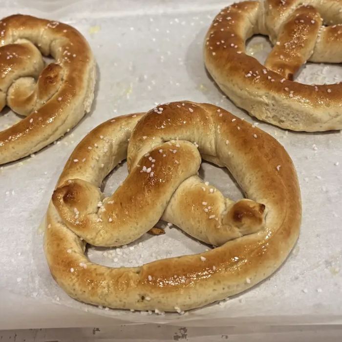 Three salted soft pretzels on a baking sheet