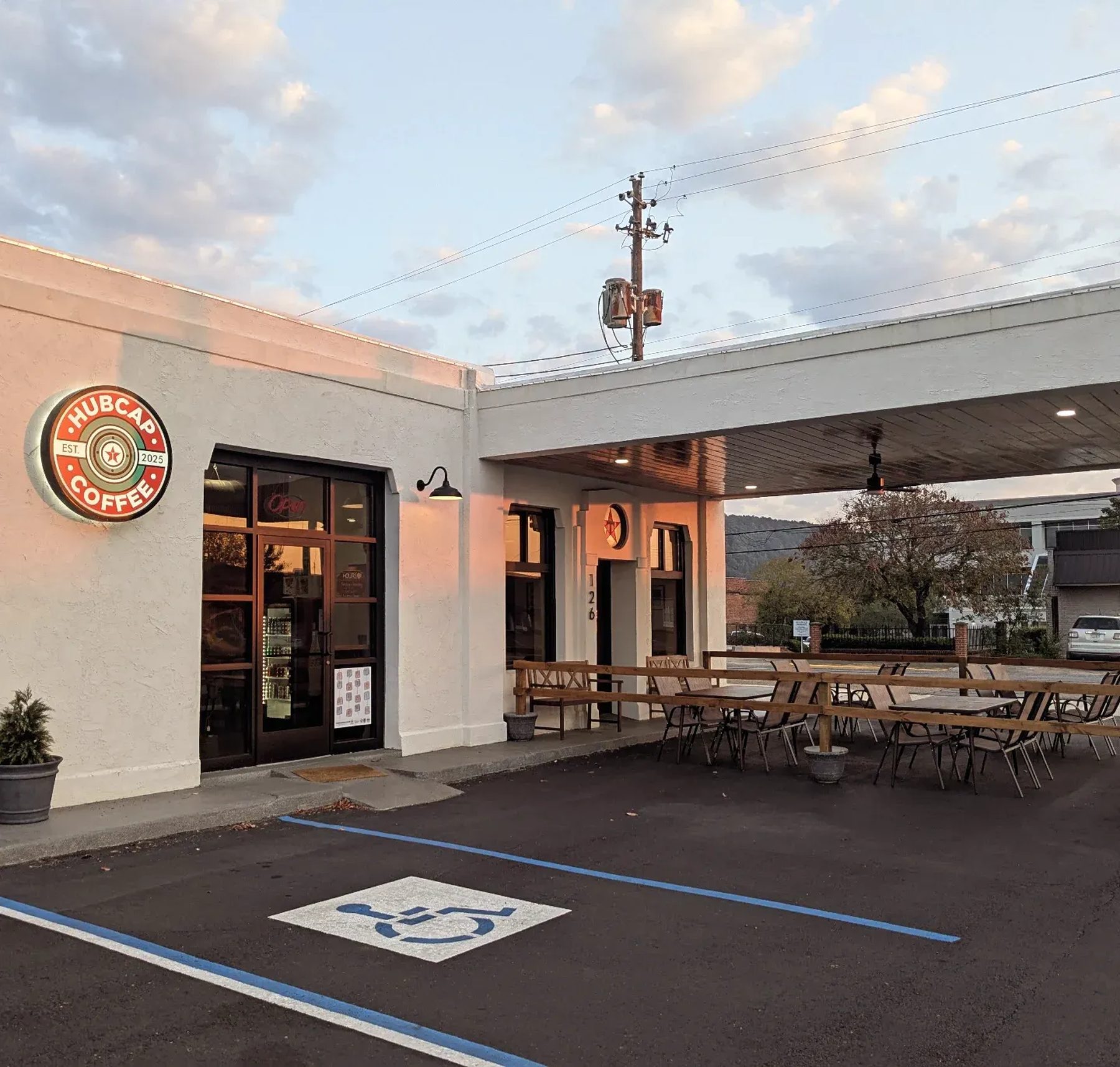 Hubcap Coffee at dusk: a white stucco former filling station with a round red and green Hubcap sign on the wall, a star over the door, and tables set out under the old pump canopy