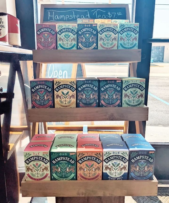 A wooden rack of Hampstead Tea boxes in the front window, with a chalkboard price sign